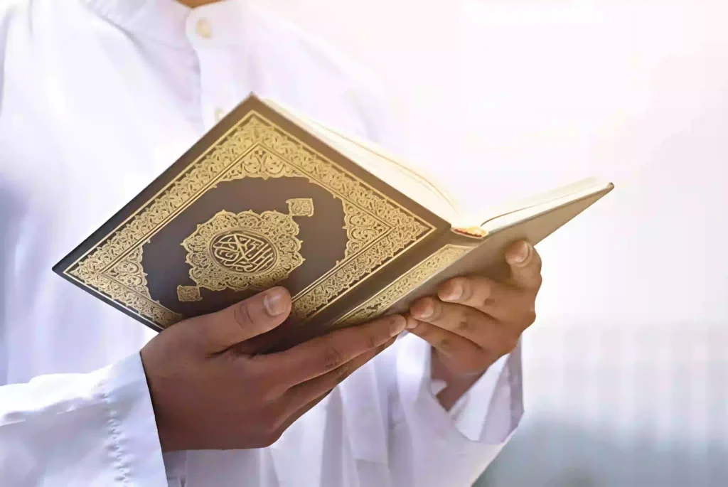 A person in white traditional clothing holds an ornate Quran, reflecting on how many hours to read the Quran to complete it during a spiritual journey.